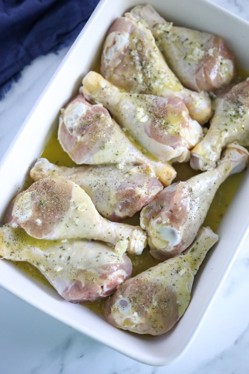 chicken drumsticks laid out in a white baking dish coated in marinade