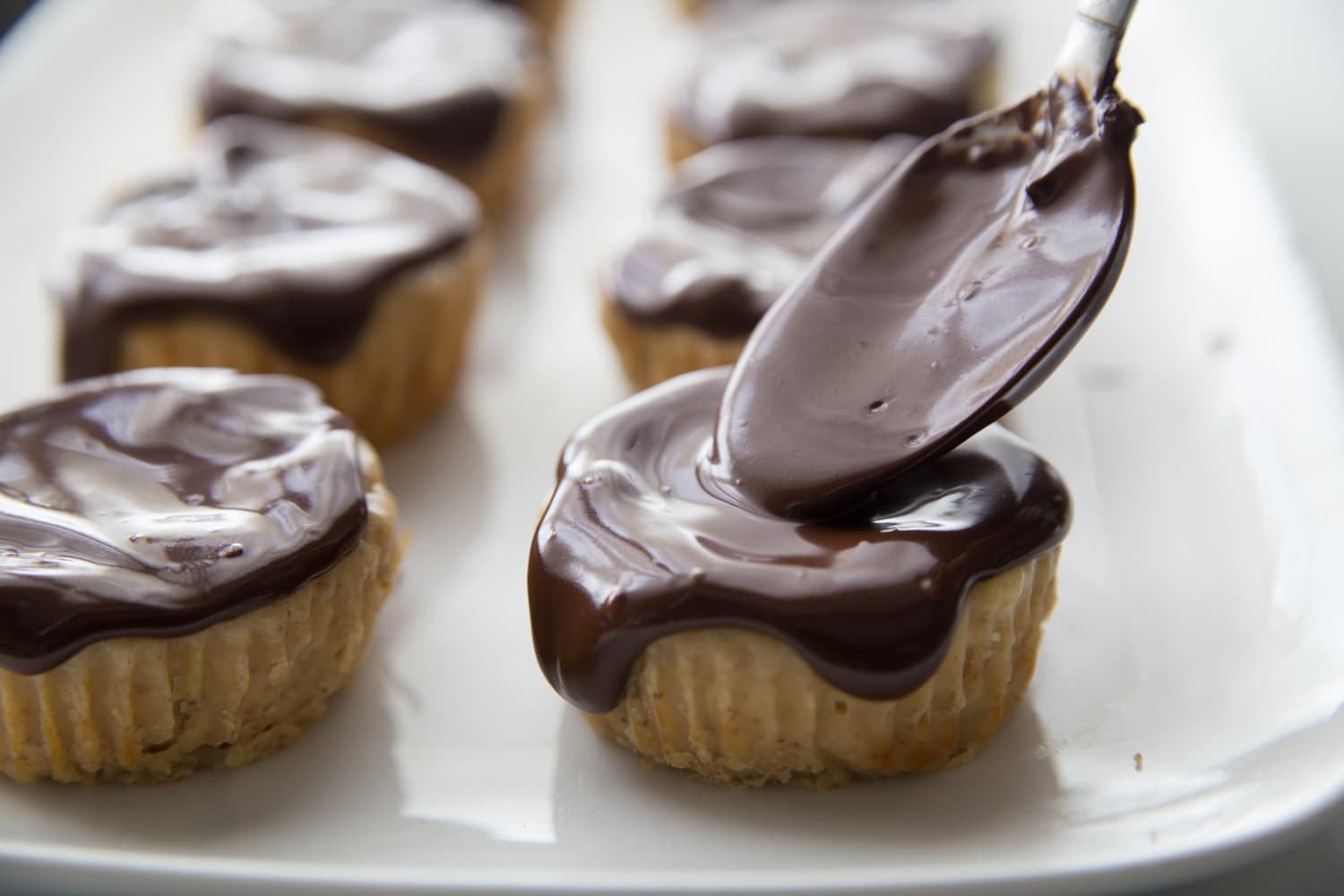 chocolate sauce being spooned over mini cheesecakes
