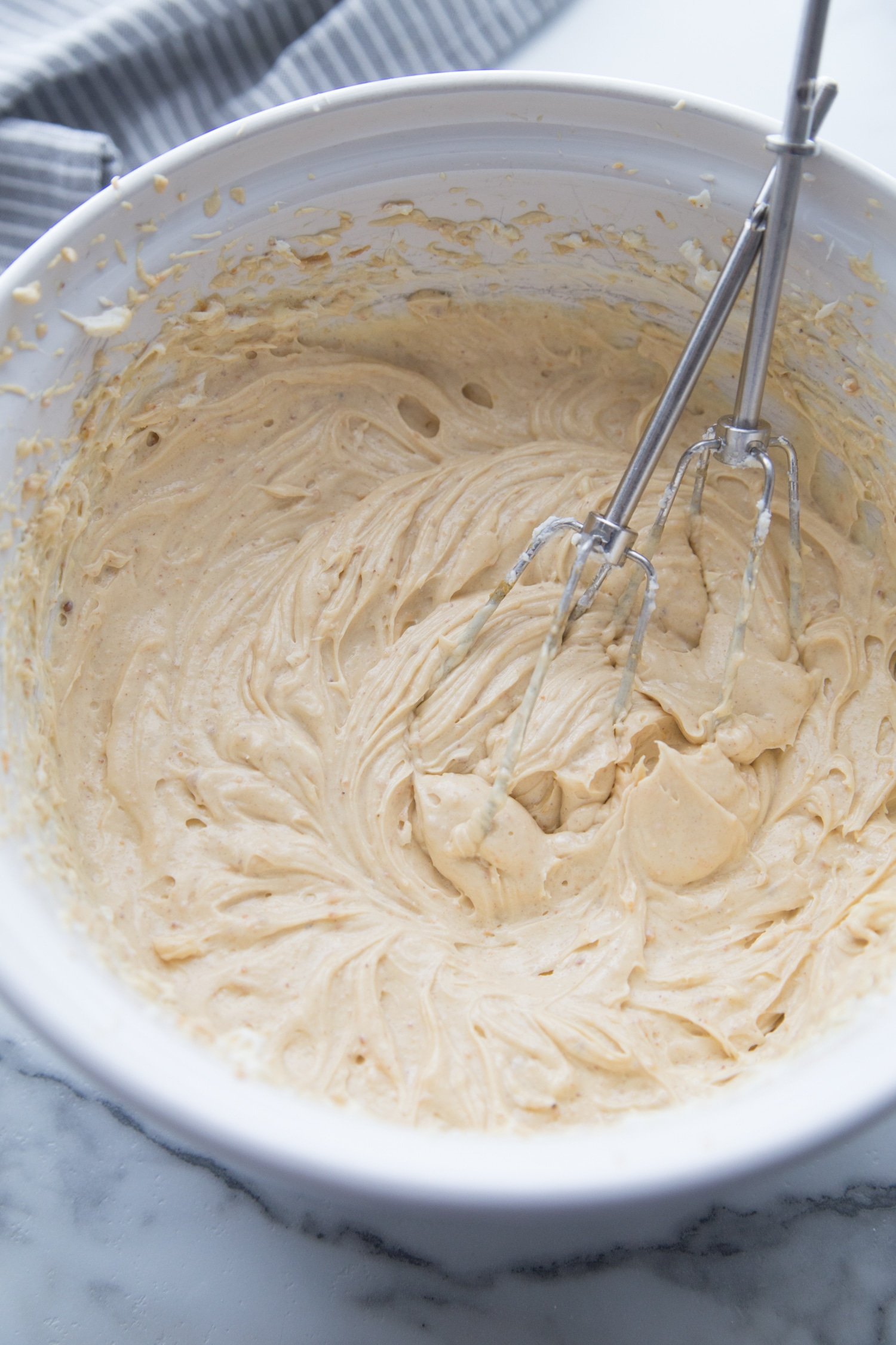 cheesecake batter mixed in a white bowl with two whisks