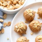 Keto Peanut Butter balls on a white plate with a small bowl of peanuts behind it