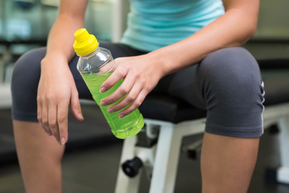 Fit woman sitting on bench holding energy drink at the gym