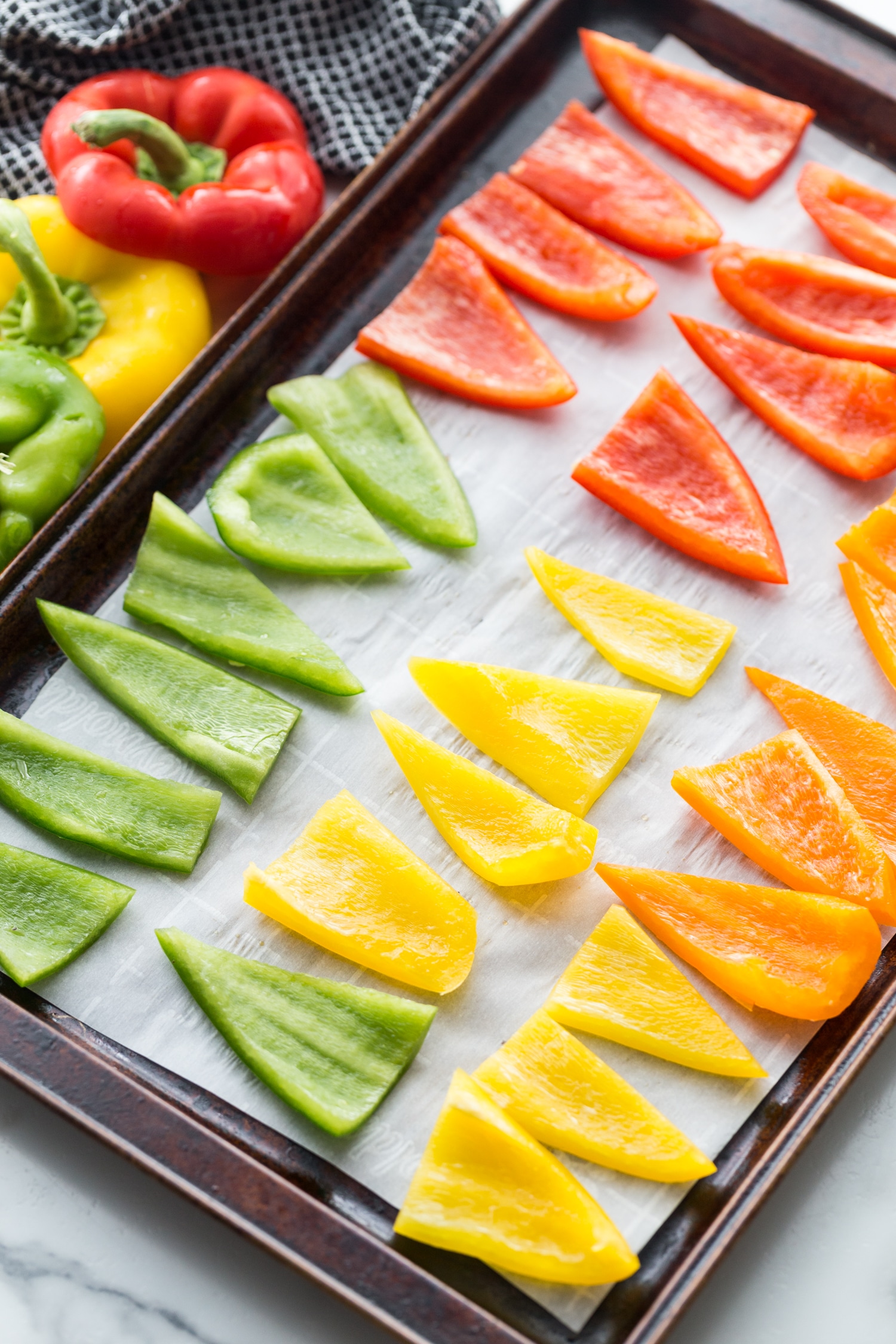 red yellow gree and orange sliced bell peppers on a baking sheet