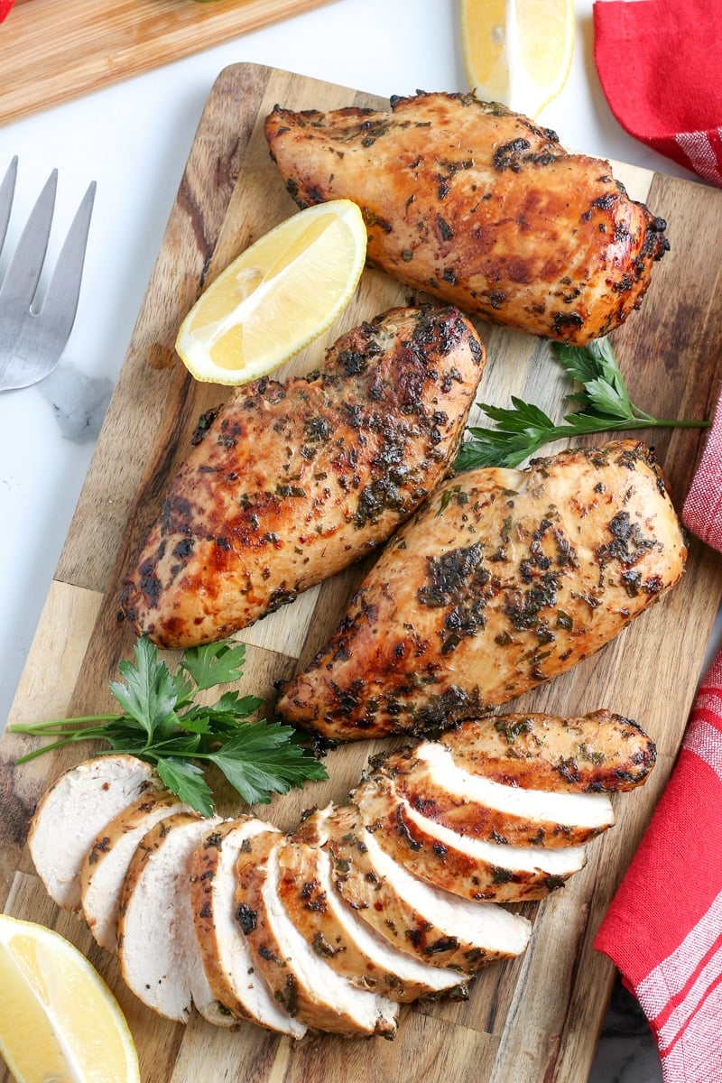 sliced air fyer chicken breasts on a cutting board with lemon and herbs