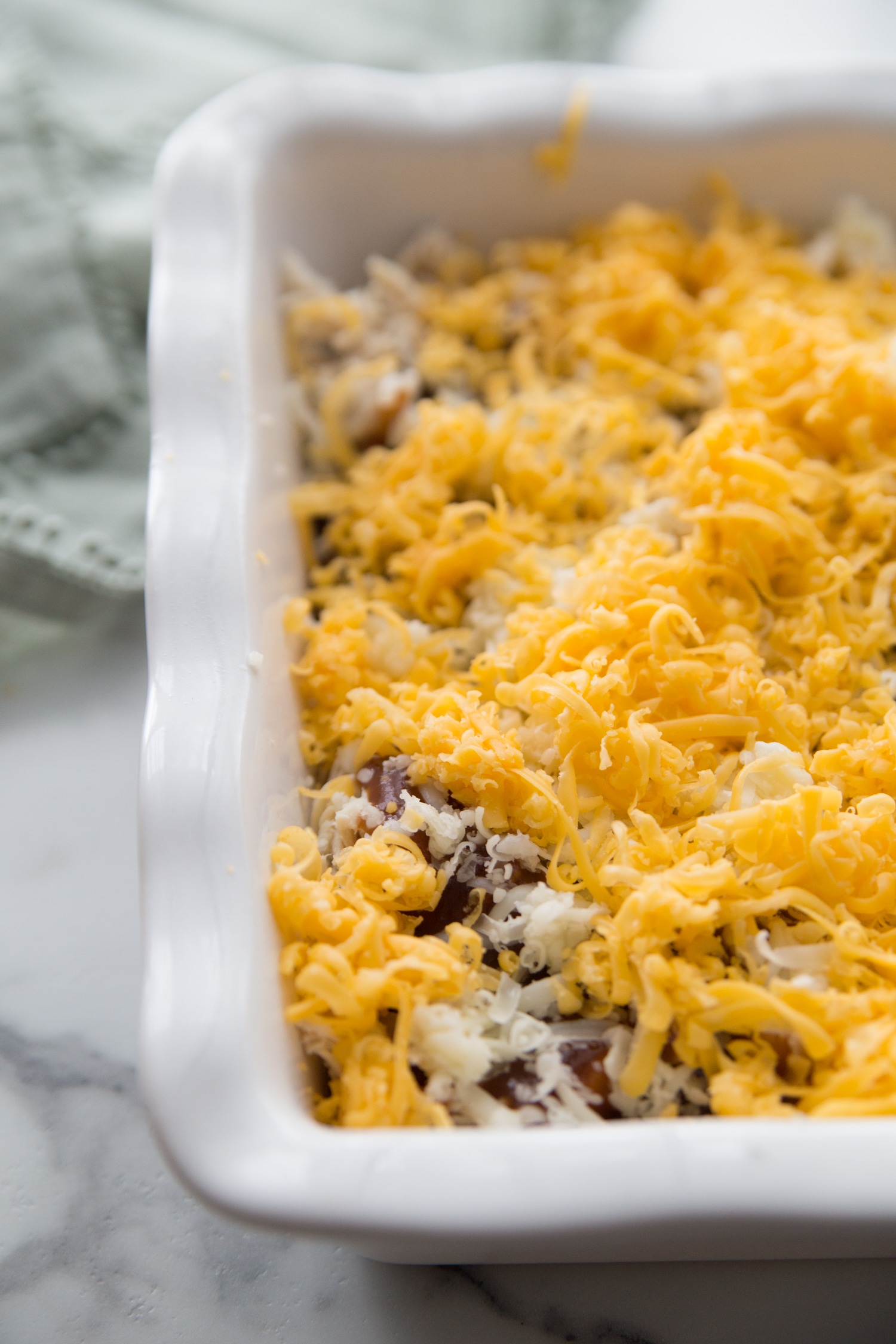 Covering bbq keto chicken casserole with shredded cheese