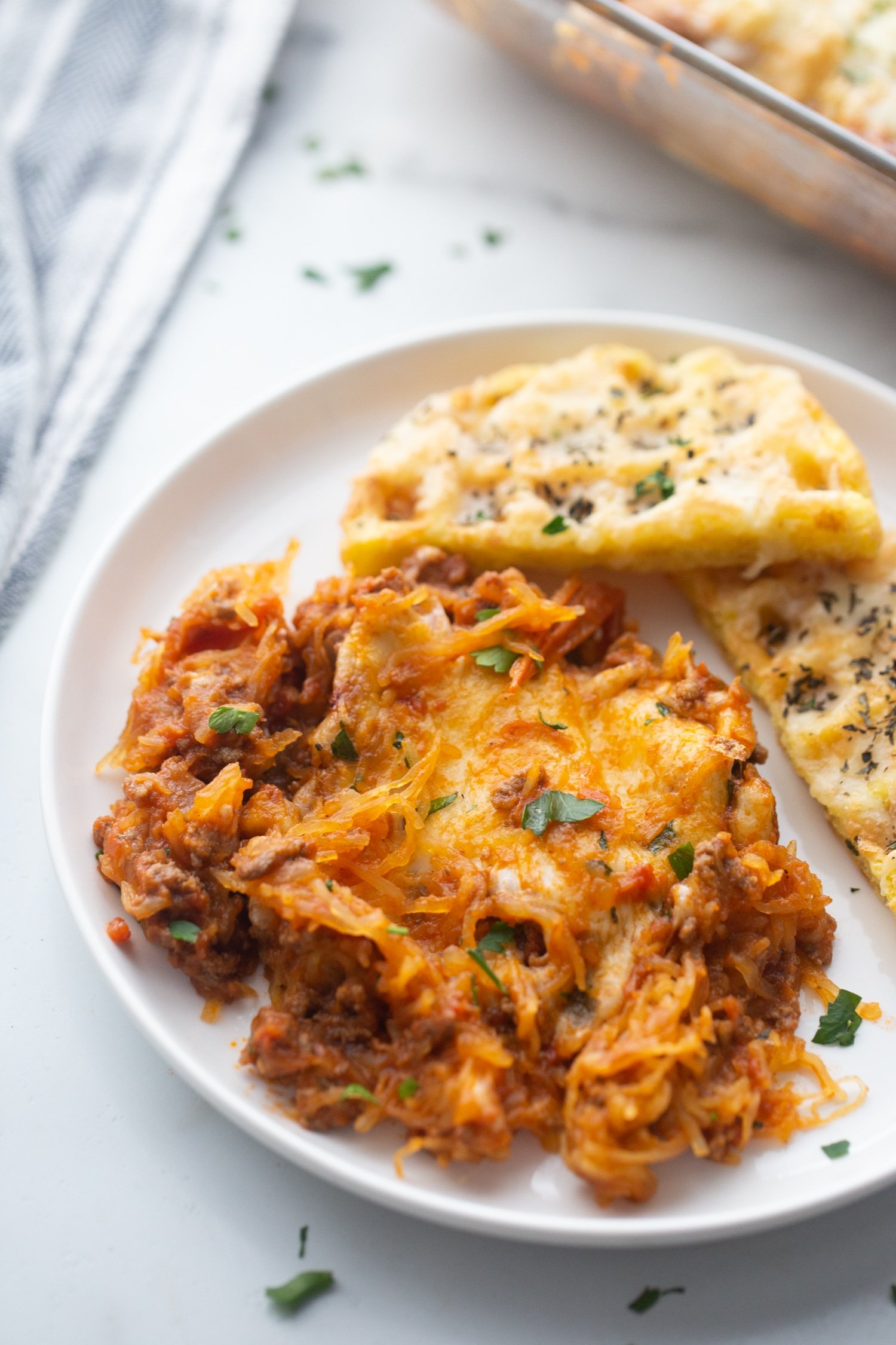keto spaghetti casserole with tender spaghetti squash, rich meat sauce, and gooey melted cheese on a plate with a low carb garlic chaffle 