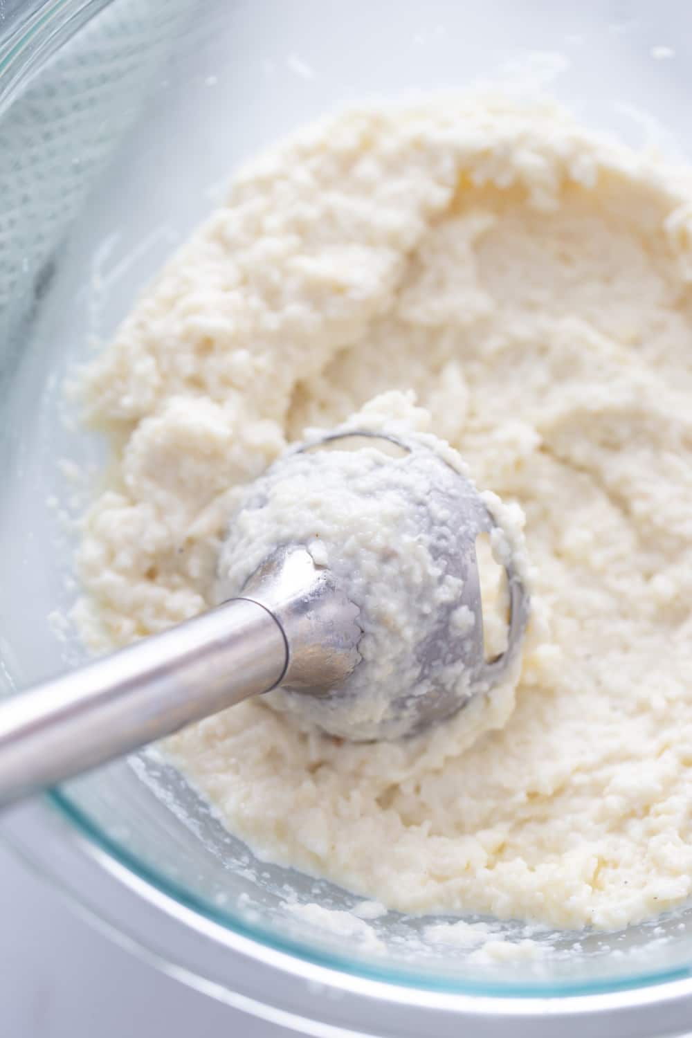blended mashed cauliflower in a glass bowl with immersion blender 