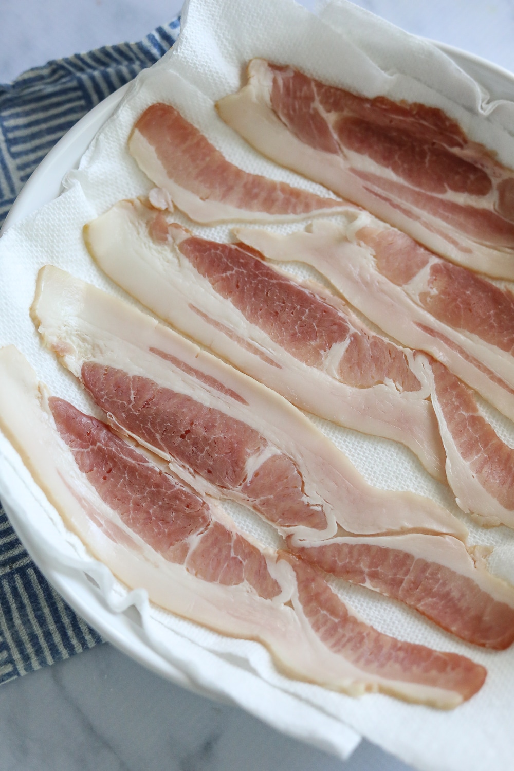 raw bacon on a white plate and paper towels.