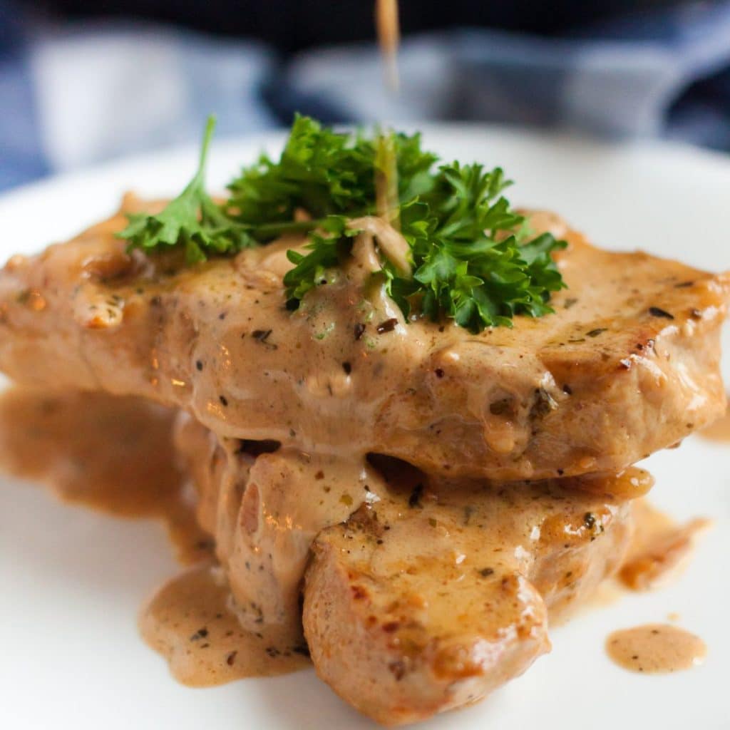 pork chops plated with sauce on top garnished with parsley