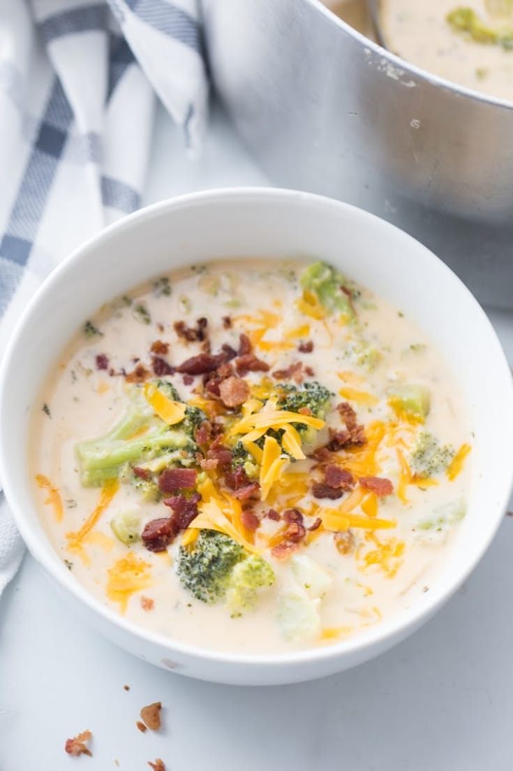 creamy instant pot broccoli cheddar soup in a white bowl garnished with bacon and grated cheese