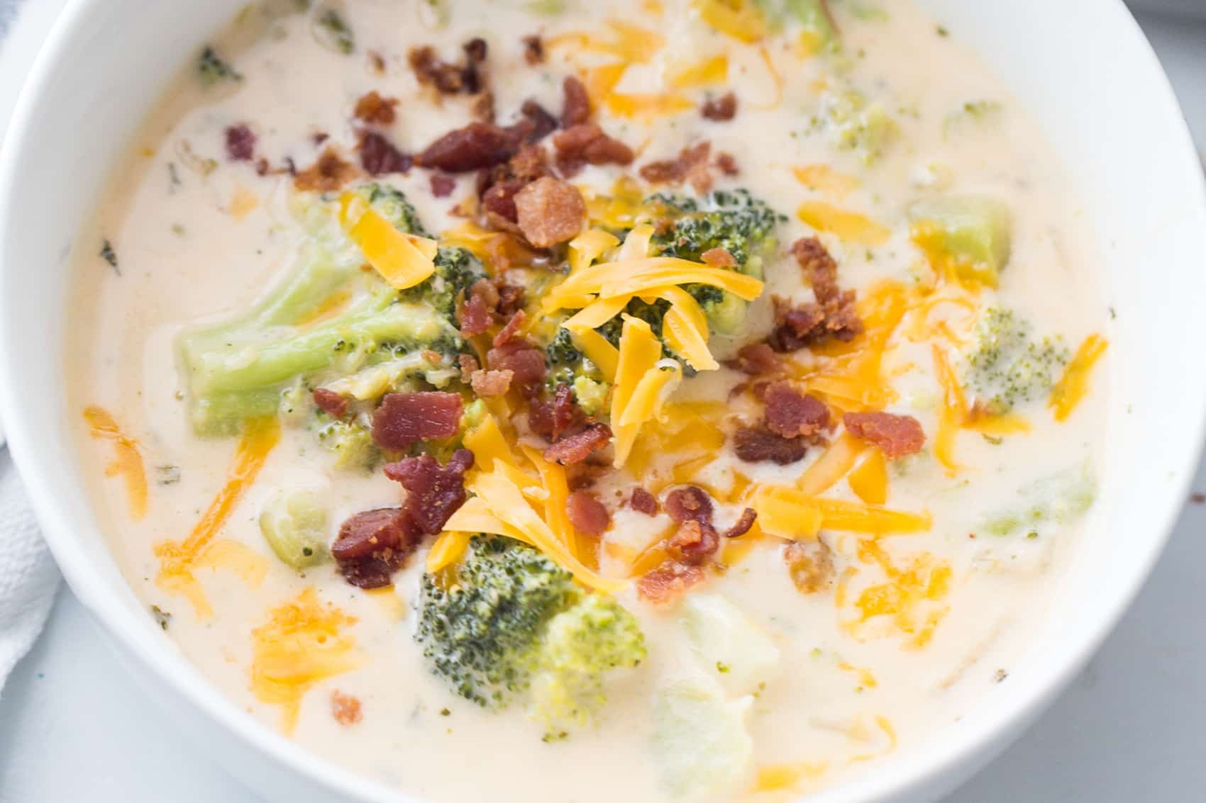 Close up of Instant Pot Broccoli Cheese Soup in a white bowl with cheese and bacon on top.