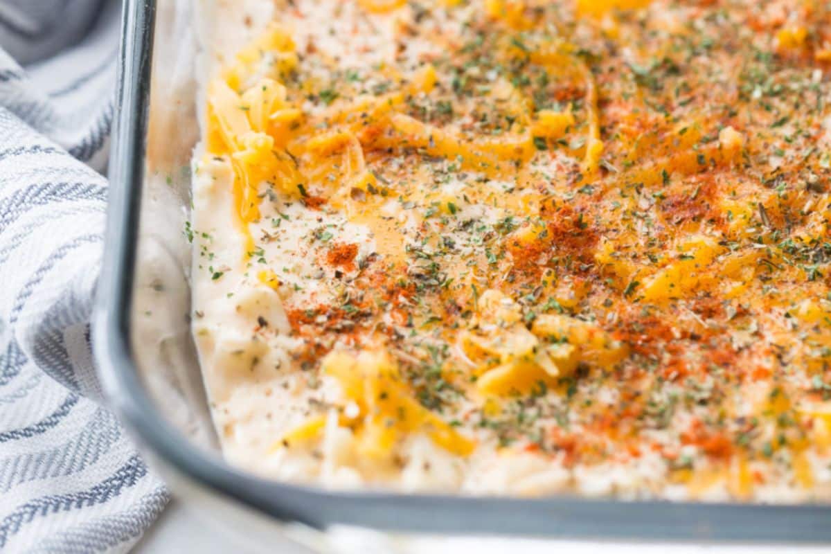 cheesy cauliflower casserole in a clear baking dish with spices on top 