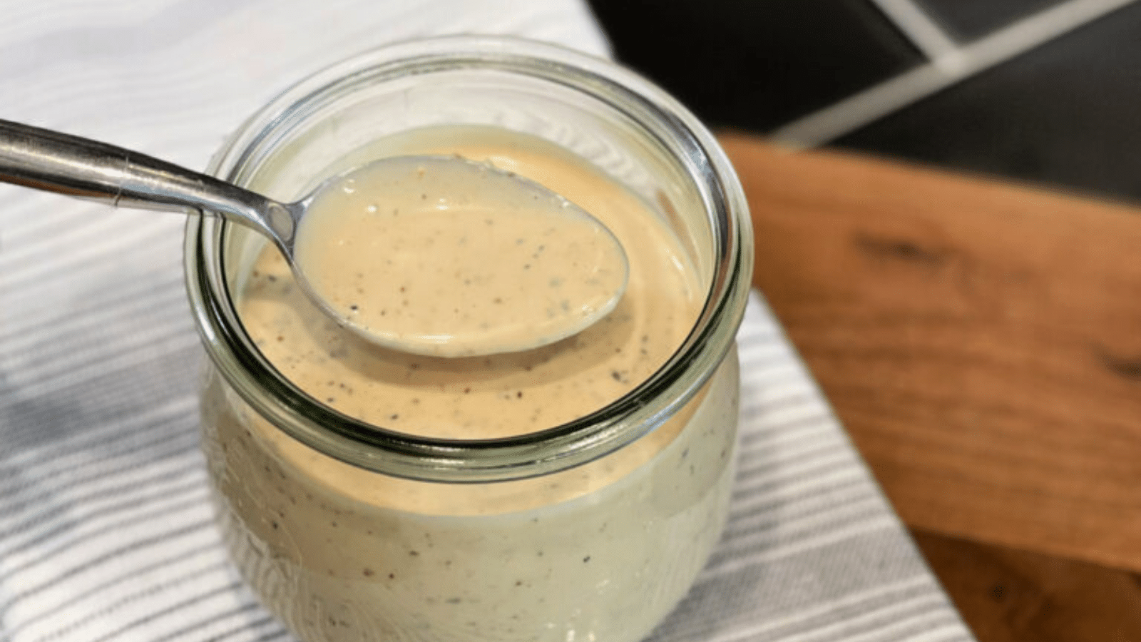 Glass jar with Alabama White BBQ Sauce and spoon dipping sauce out of jar