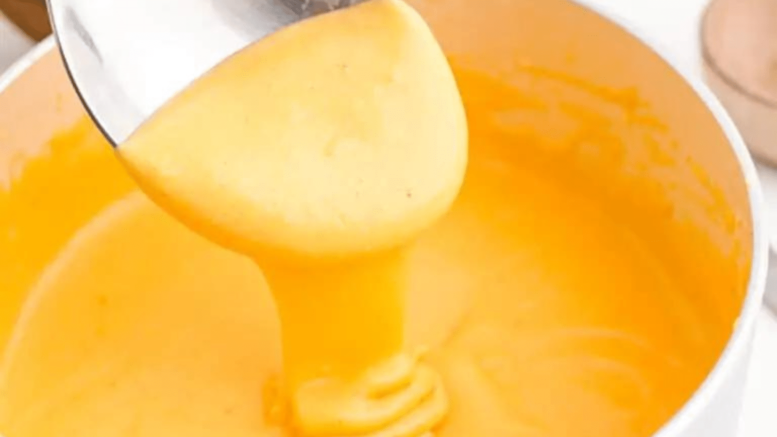 Close up of spoon with beer cheese drizzling cheese into pot
