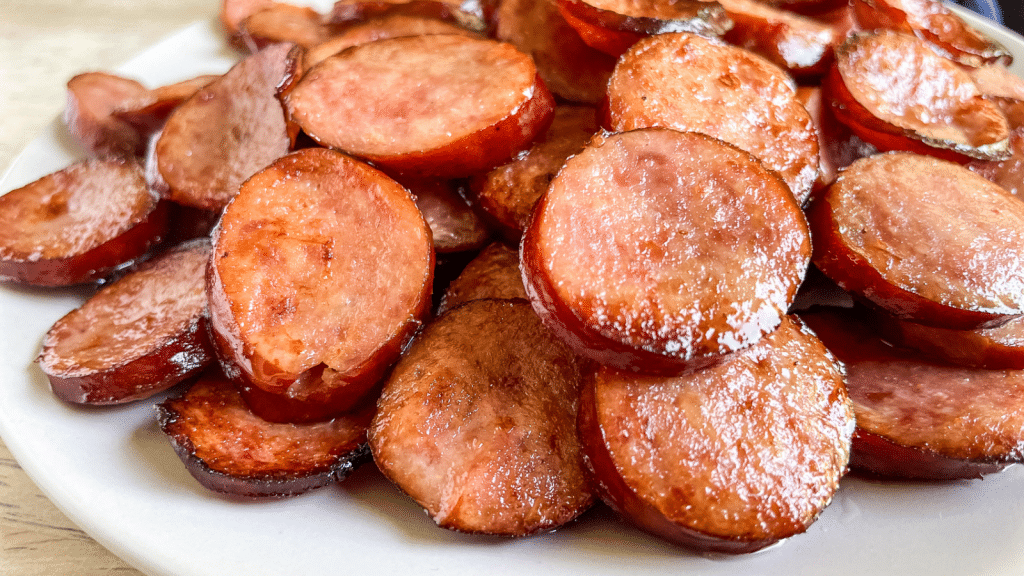 Close up photo of sliced smoked sausage links after being air fried, showing the browned, crispy exterior and cooked through interiors of the low carb high protein sausage pieces on a white plate.