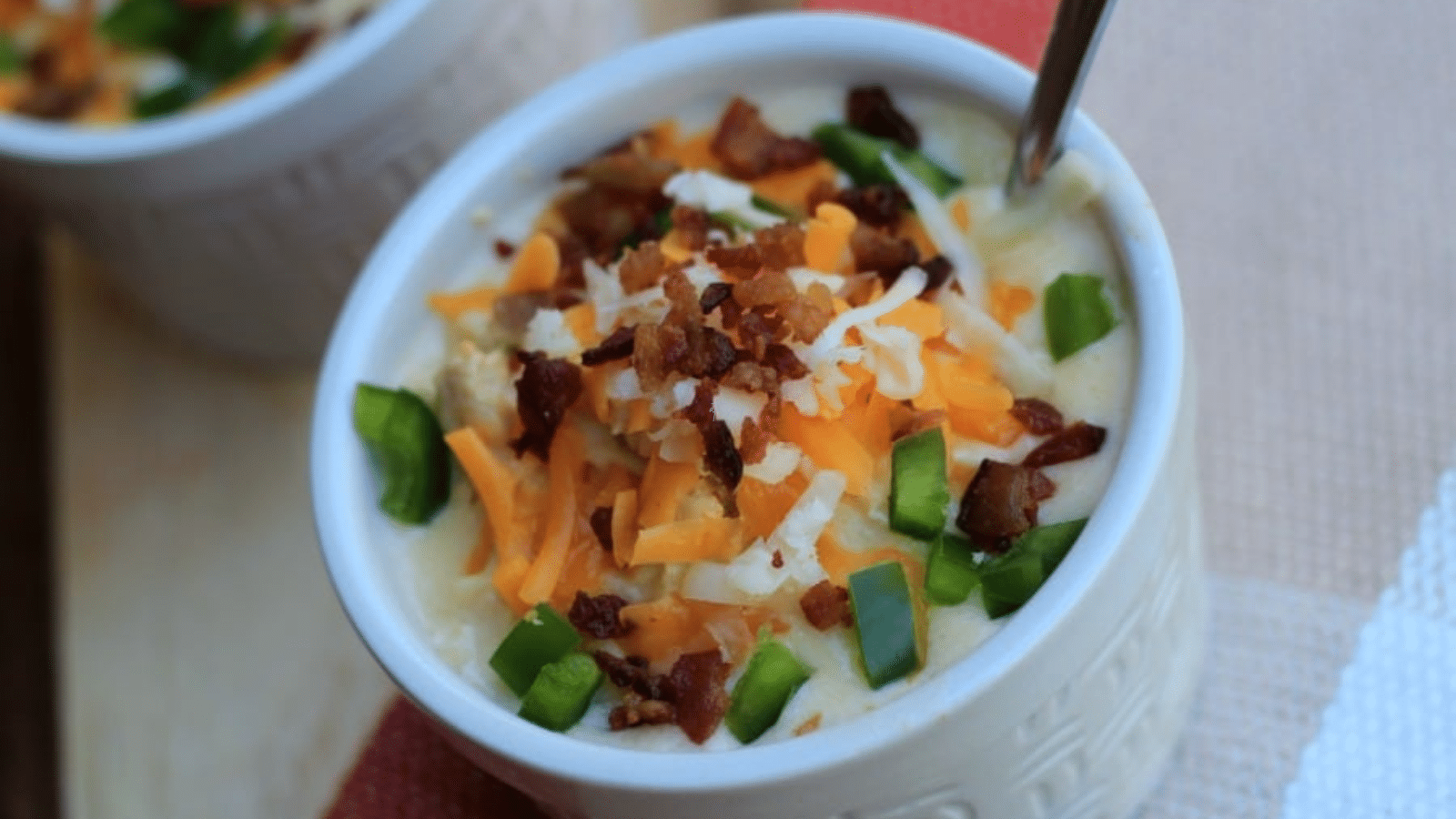 Close up of jalapeno popper soup in white bowl with cheese bacon and scallions