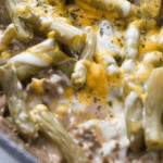 Extreme close-up view inside the cast iron skillet showcasing the gooey and delicious layers of keto friendly ground beef casserole featuring beans, beef broth sauce, cheddar cheese, and savory seasonings before going in the oven