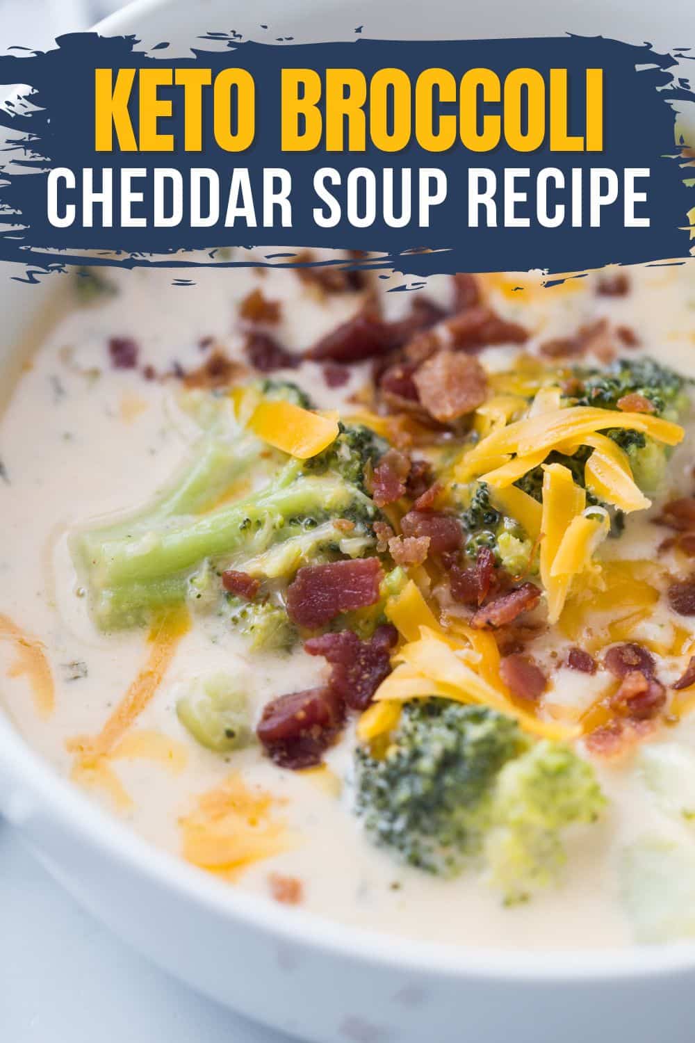 a white bowl of keto broccoli and cheese soup garnished with bacon and freshly shredded cheese
