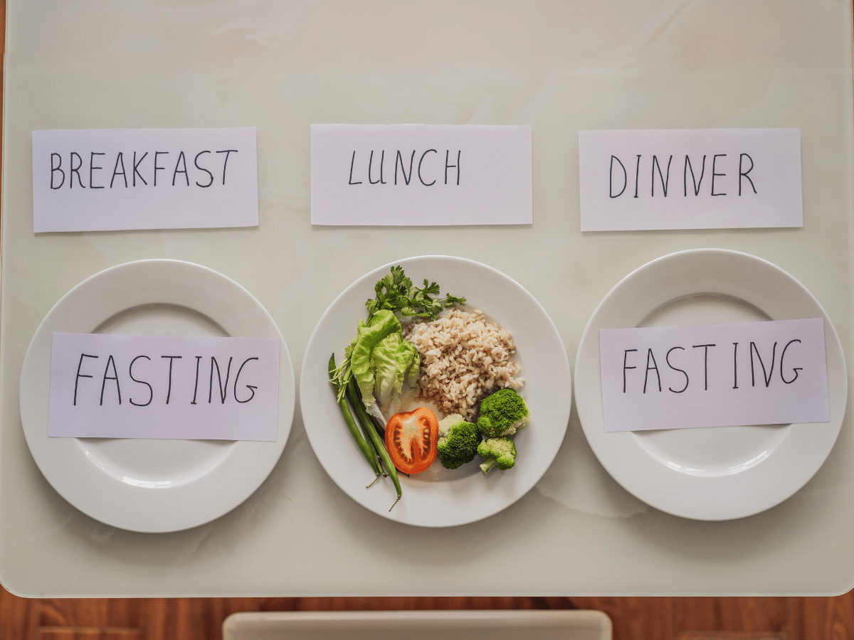 2 plates with word fasting surrounds plate with food between