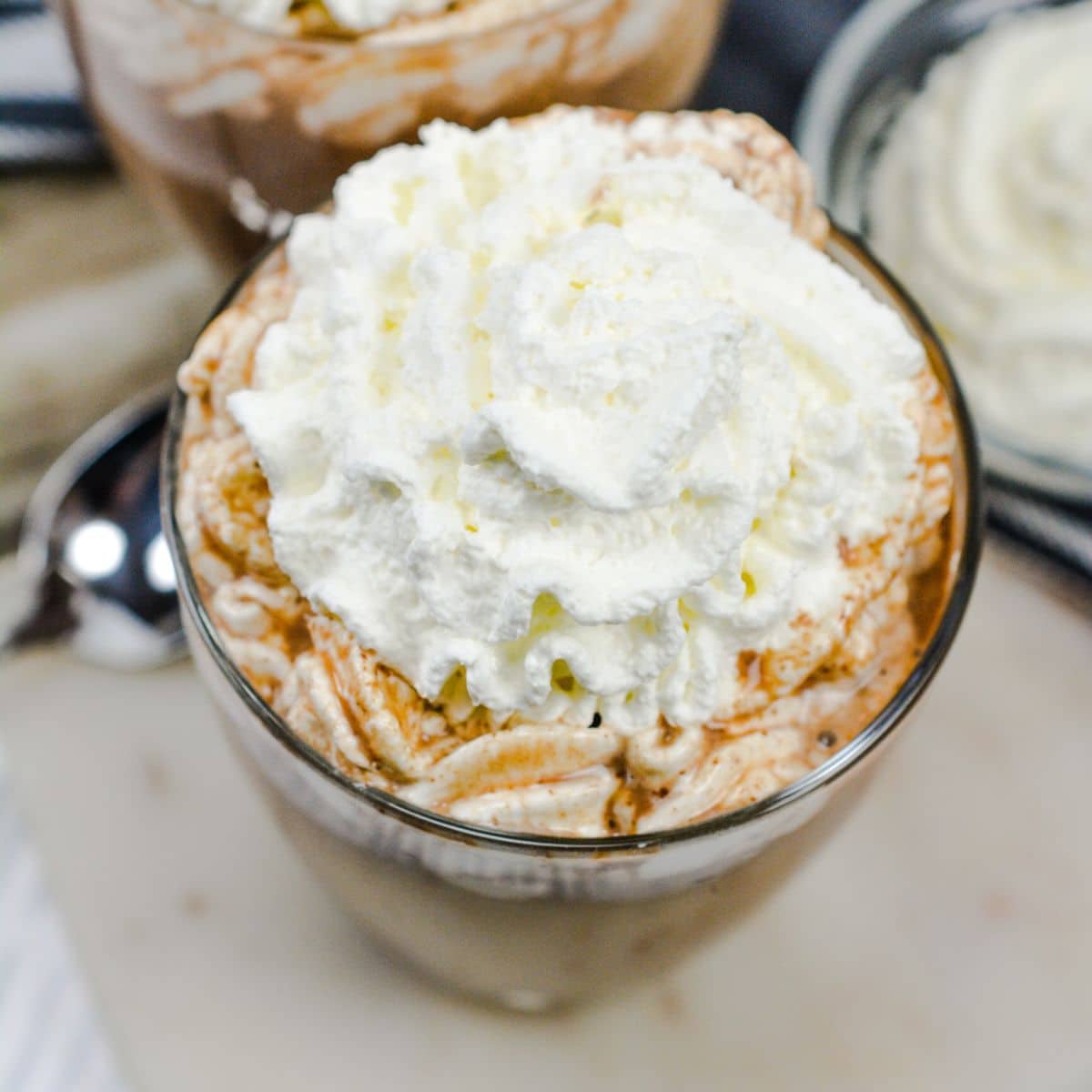 Square image of keto friendly sugar free hot chocolate served in clear glass and topped with whipped cream.