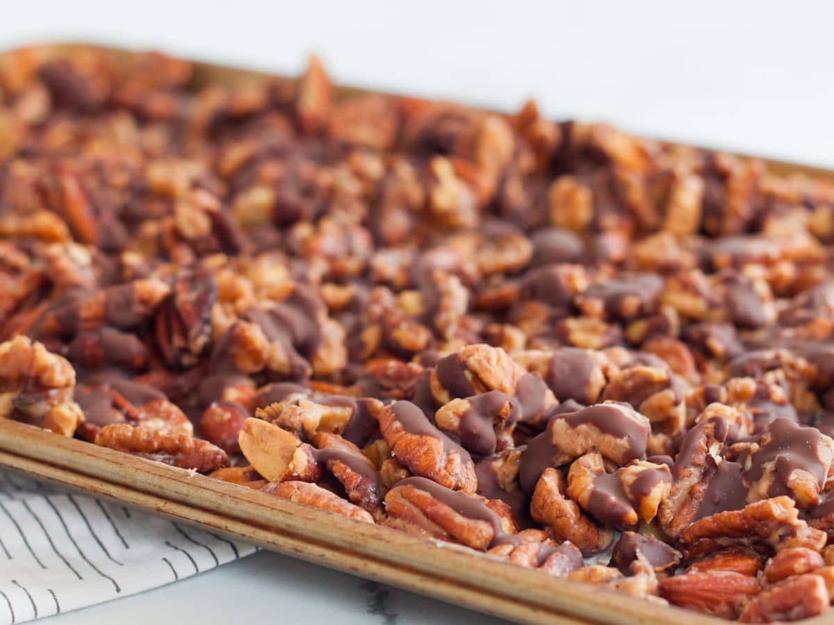 baking sheet with candied pecans drizzled with chocolate on a white background and a kitchen linen