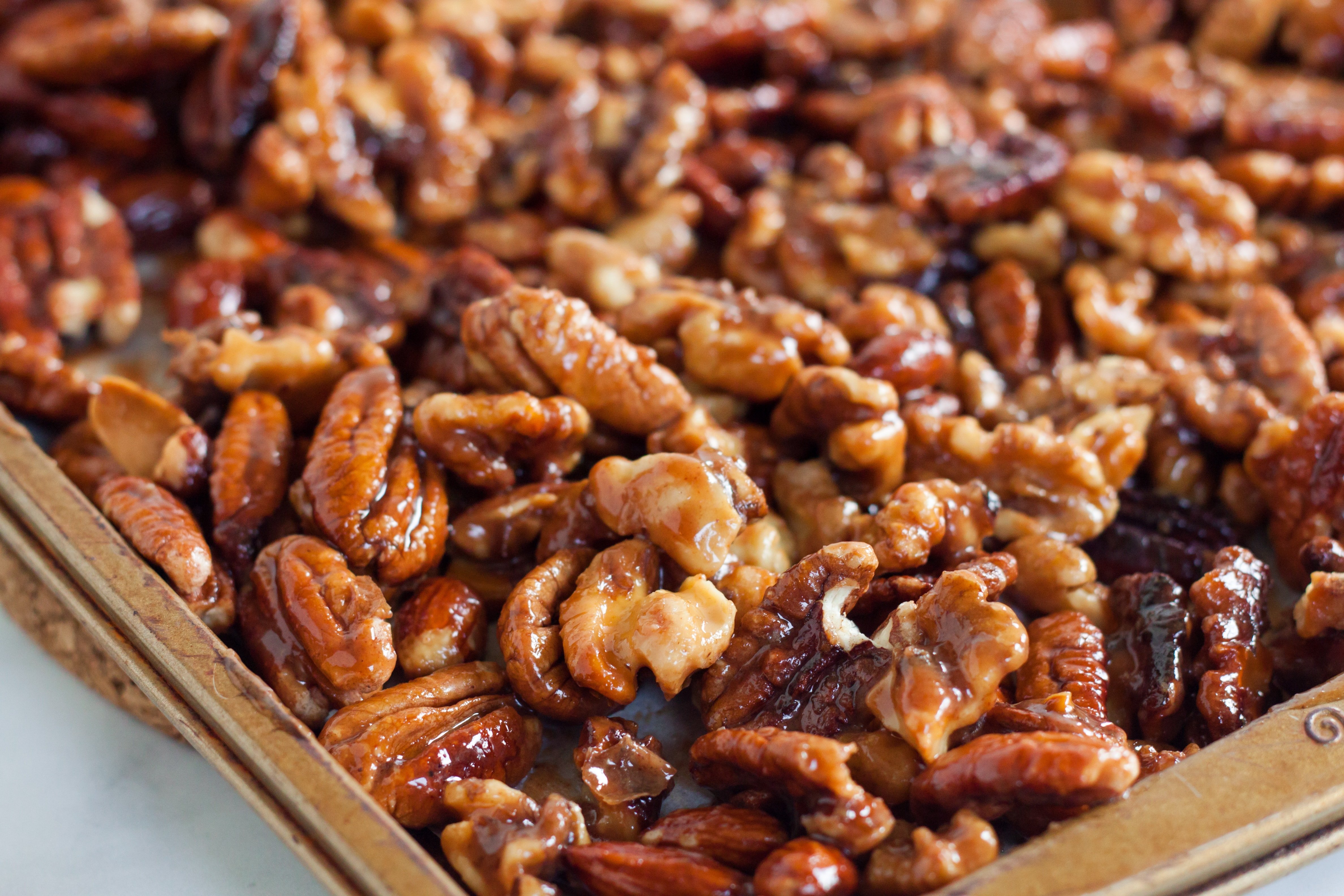 Baking sheet with almonds, walnuts, and pecans spread evenly with a drizzle of coconut oil and sweetener.