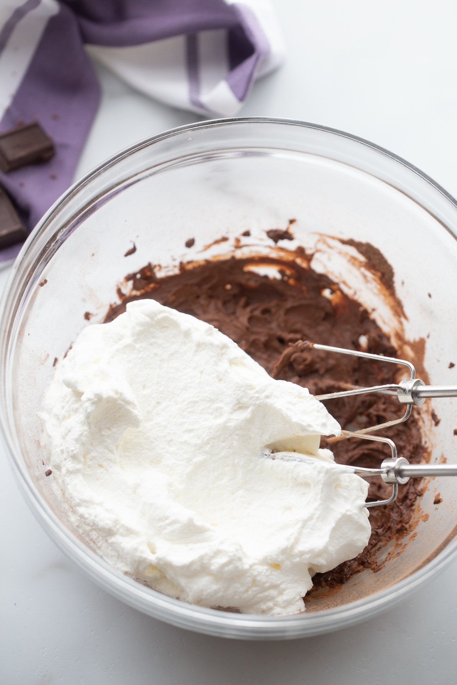 Image of whipped cream mixture being folded into chocolate mouse in glass mixing bowl