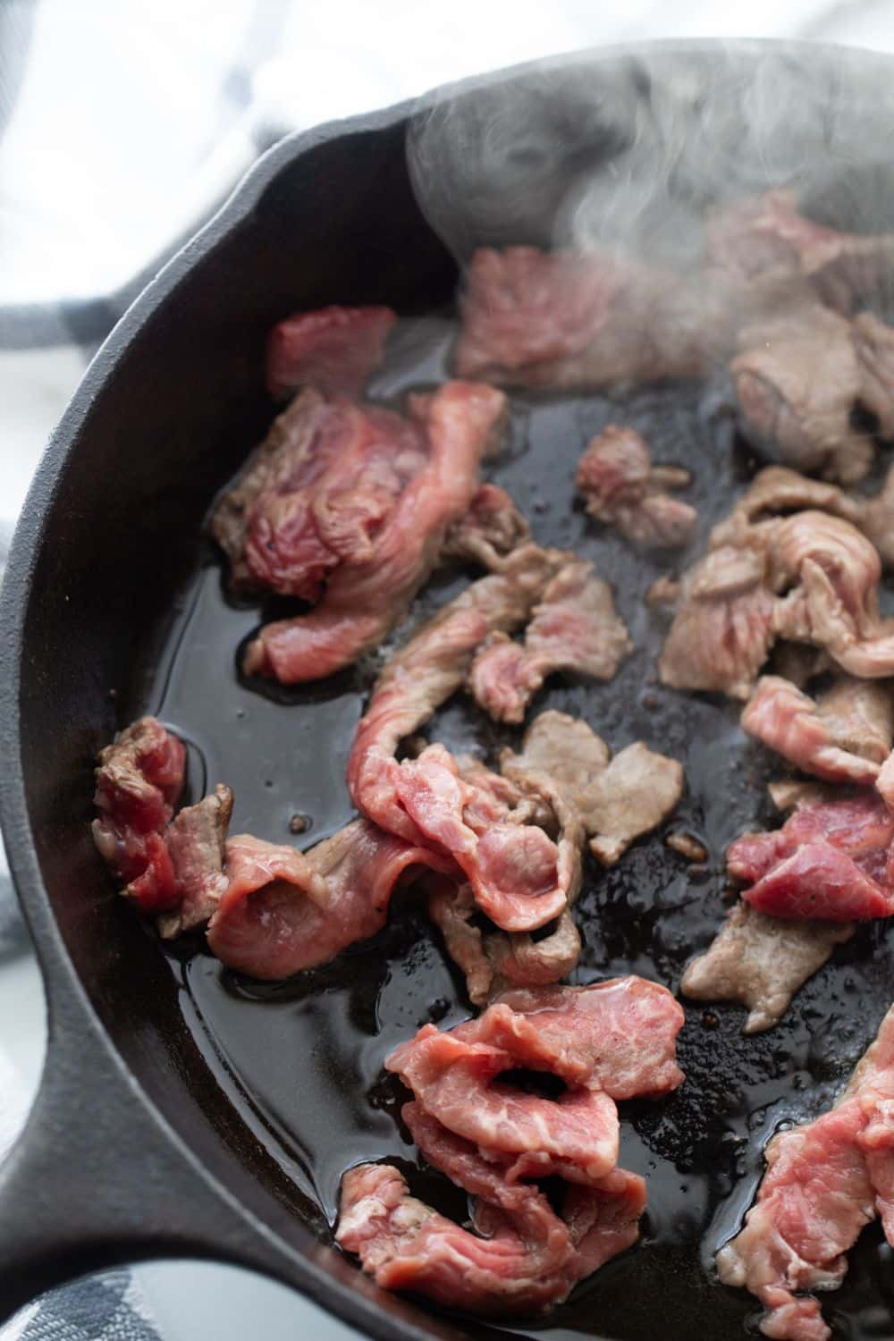 Image of cast iron skillet with browning cubes of steak.
