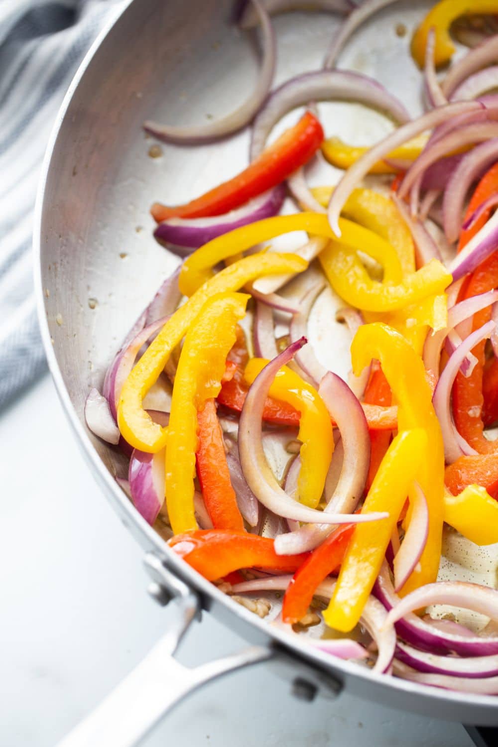 image of sliced onion and yellow and red peppers being cooked in a metal skillet