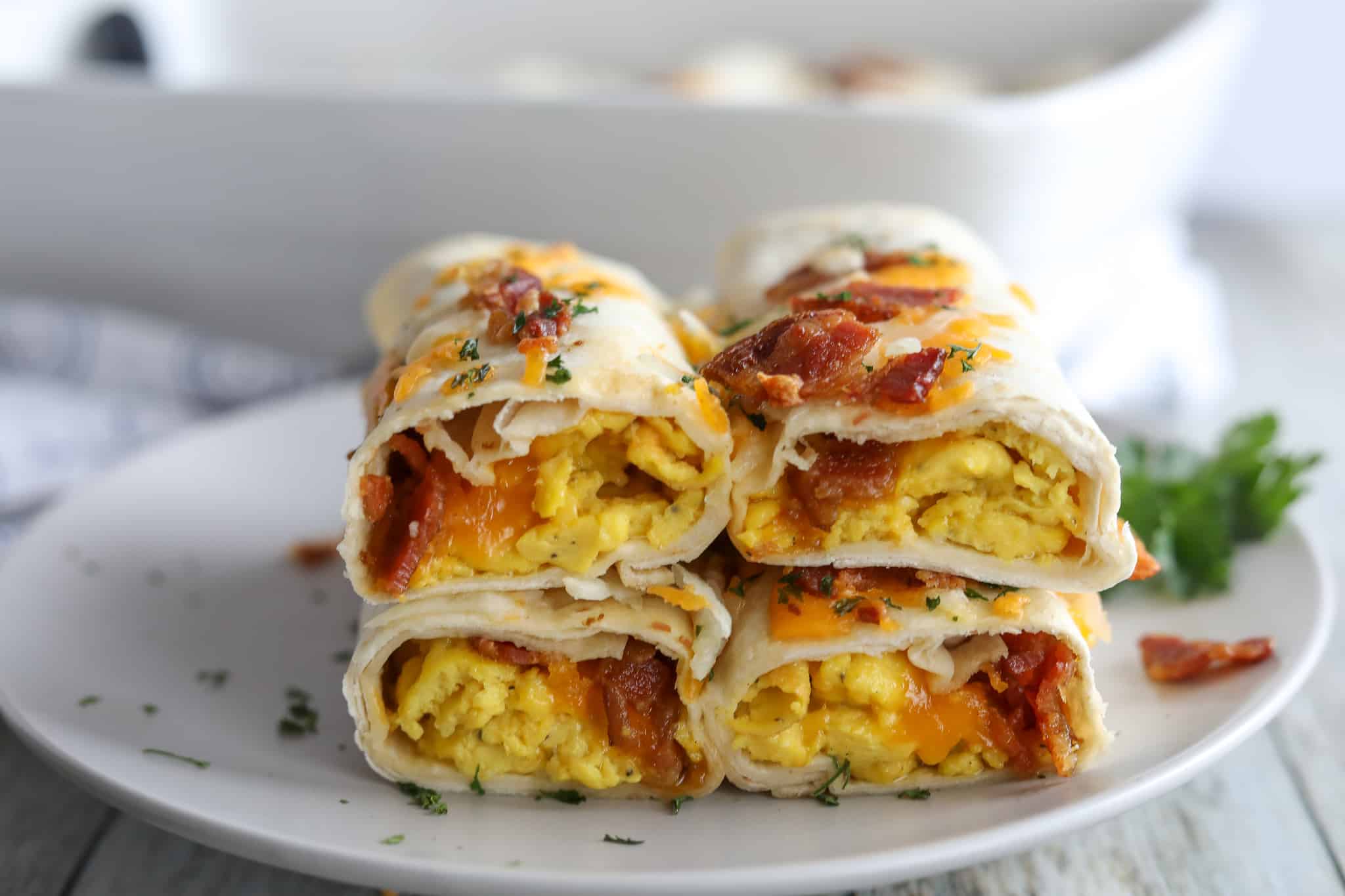 freezer friendly breakfast burritos with bacon eggs and cheese on a white plate with a casserole dish in the background 