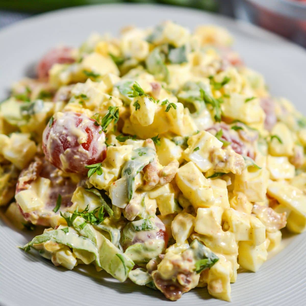 Overhead view of creamy keto egg salad topped with crispy bacon pieces, chopped egg, tomato and chives ready to enjoy as a high protein low carb meal