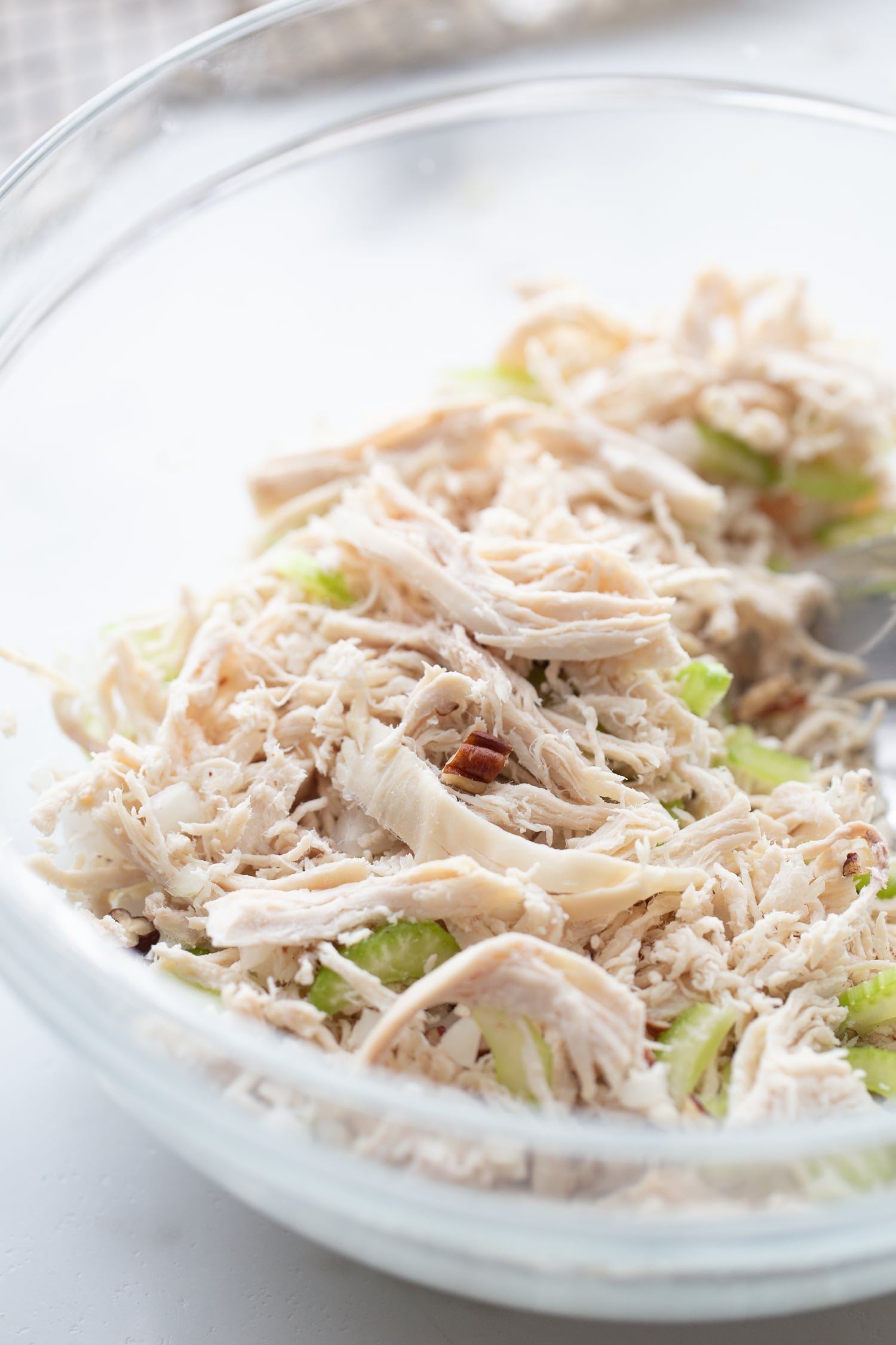 Close-up photo of shredded chicken, chopped pecans, and diced celery being mixed together in a glass mixing bowl for keto chicken salad recipe