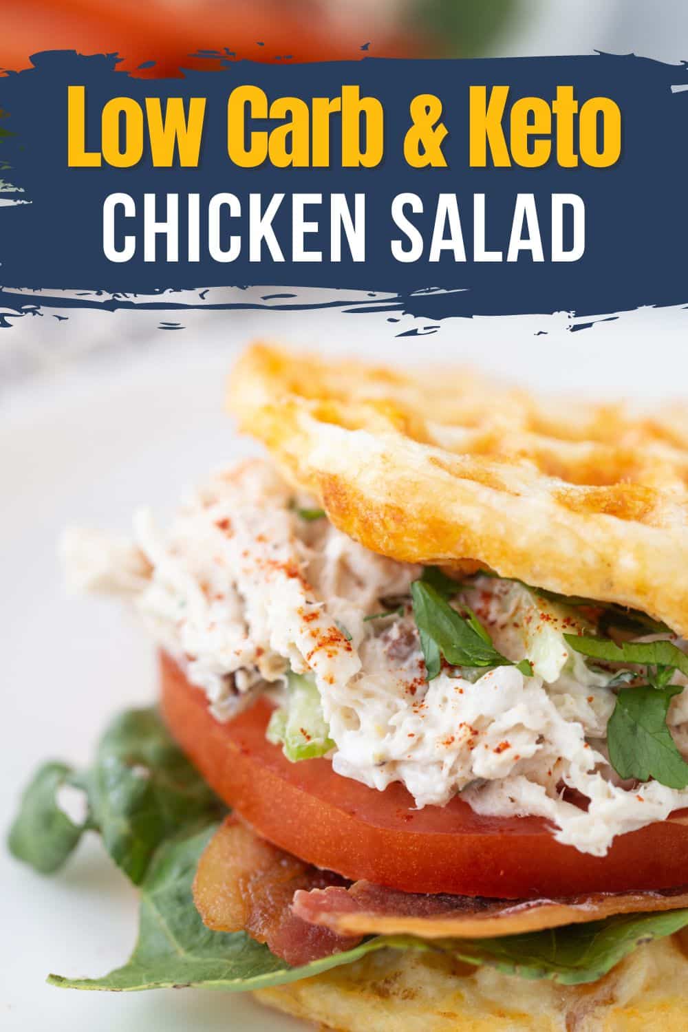 Keto chicken salad lettering banner over sandwich stuffed with shredded chicken, pecans, celery, tomato, bacon, lettuce, parsley between chaffles