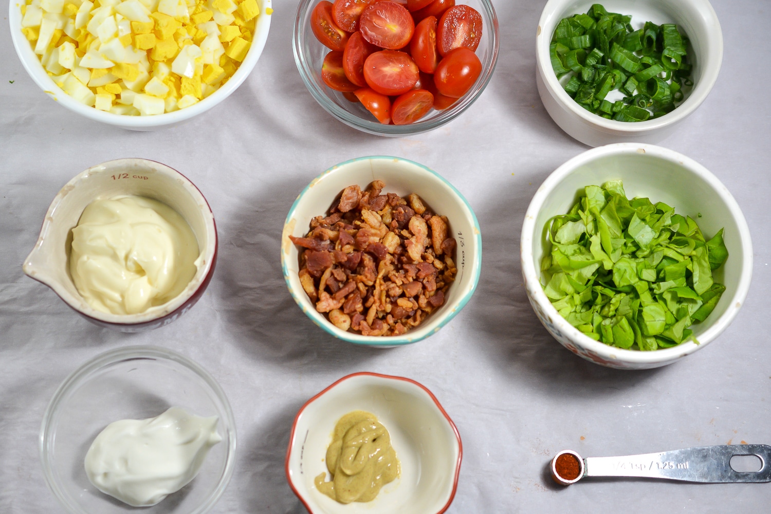 Overhead shot of all prepared ingredients for making keto egg salad including chopped hard boiled eggs, crumbled bacon, halved cherry tomatoes, butter lettuce, chopped onion, mayonnaise, mustard and seasonings