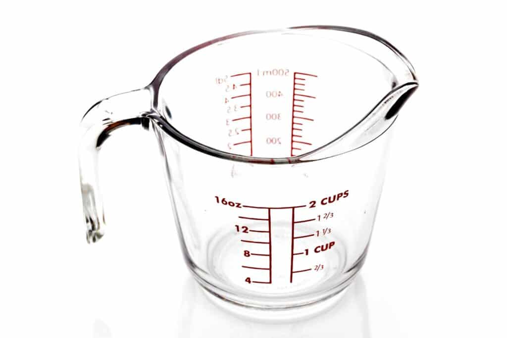 Glass measuring cup with spout and handle on a white background with markings up the side denoting measurements of cups and ounces