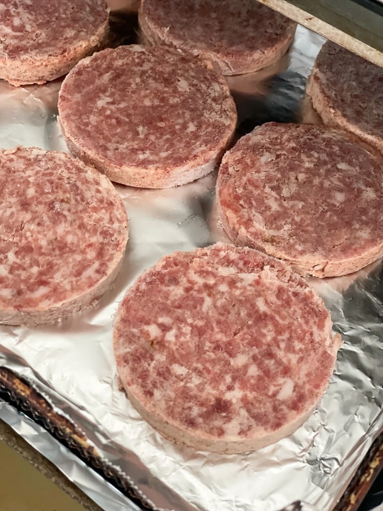 Overhead view of raw sausage patties arranged in a single layer on aluminum foil lining an air fryer pan.