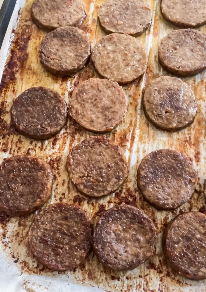 Overhead view of a sheet pan with perfectly cooked sausage patties arranged in neat rows on a baking tray lined with parchment paper.