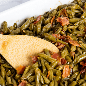 Stirring the fully baked crack green beans casserole with a wooden spoon, showcasing the irresistible texture and perfect consistency of the dish.