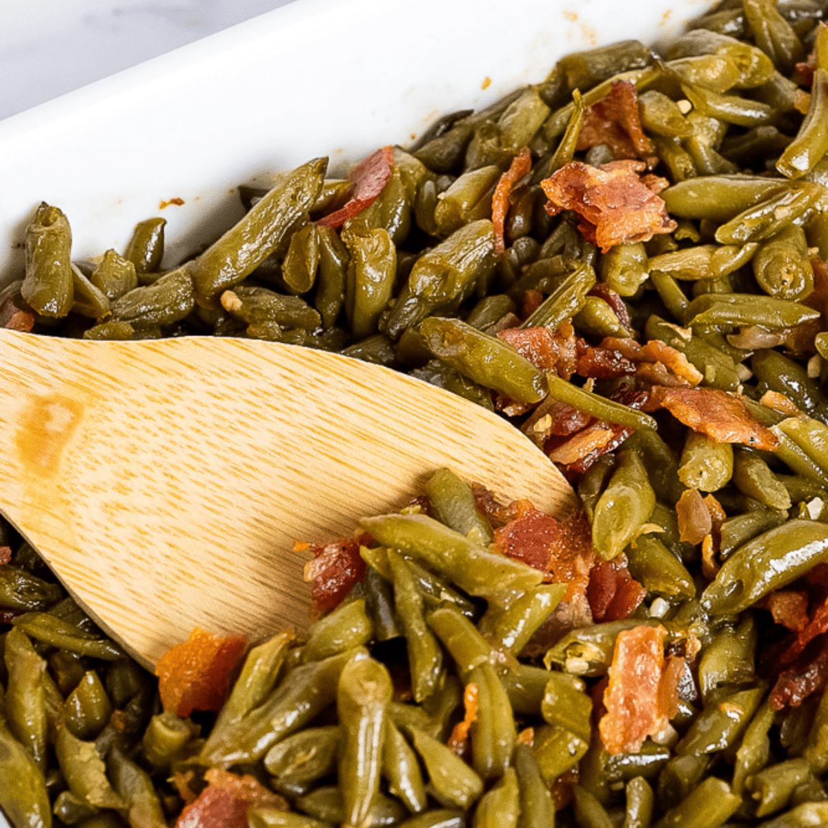 Stirring the fully baked crack green beans casserole with a wooden spoon, showcasing the irresistible texture and perfect consistency of the dish.