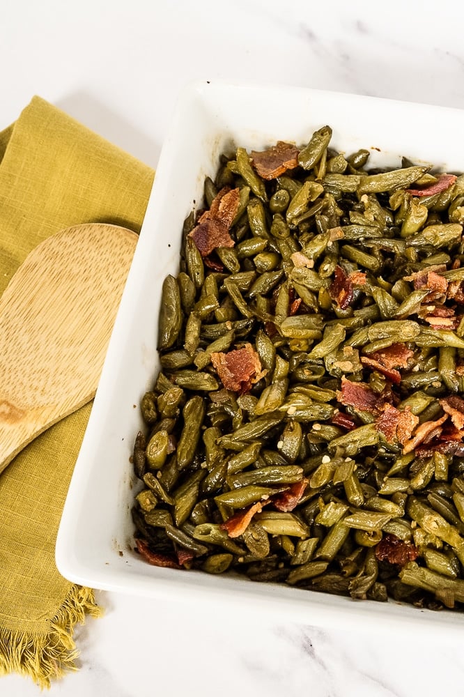 The fully baked crack green beans casserole served in a white casserole dish, presented on a white background with a yellow serving cloth for a visually appealing and enticing final dish.
