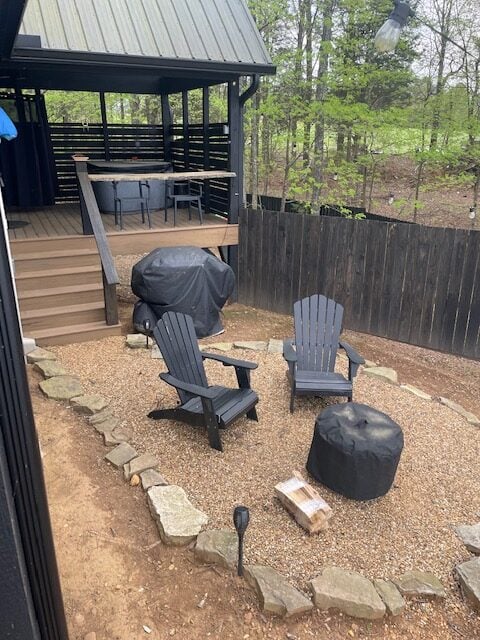 view of outside of cabin. 2 chairs and fire pit in the forefront. Dining area, hot tub, and outdoor shower in background.