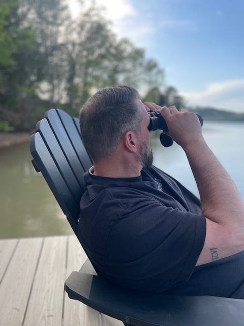 man looking through binoculars sitting on dock.