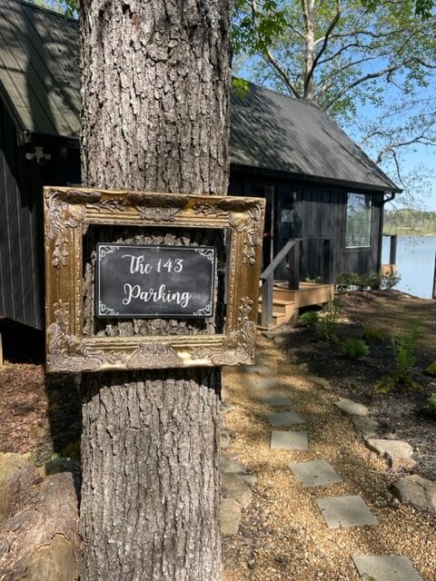 Outside of cabin with large tree in front. sign hanging on tree says The 143.