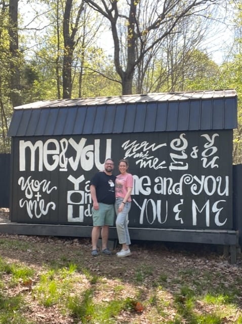 2 people standing in front of a barn with cute writing and sayings on it. 