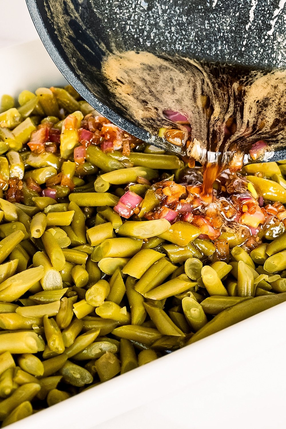Pouring the flavorful bacon and seasoning mixture over the arranged green beans to create the irresistible crack green beans casserole.