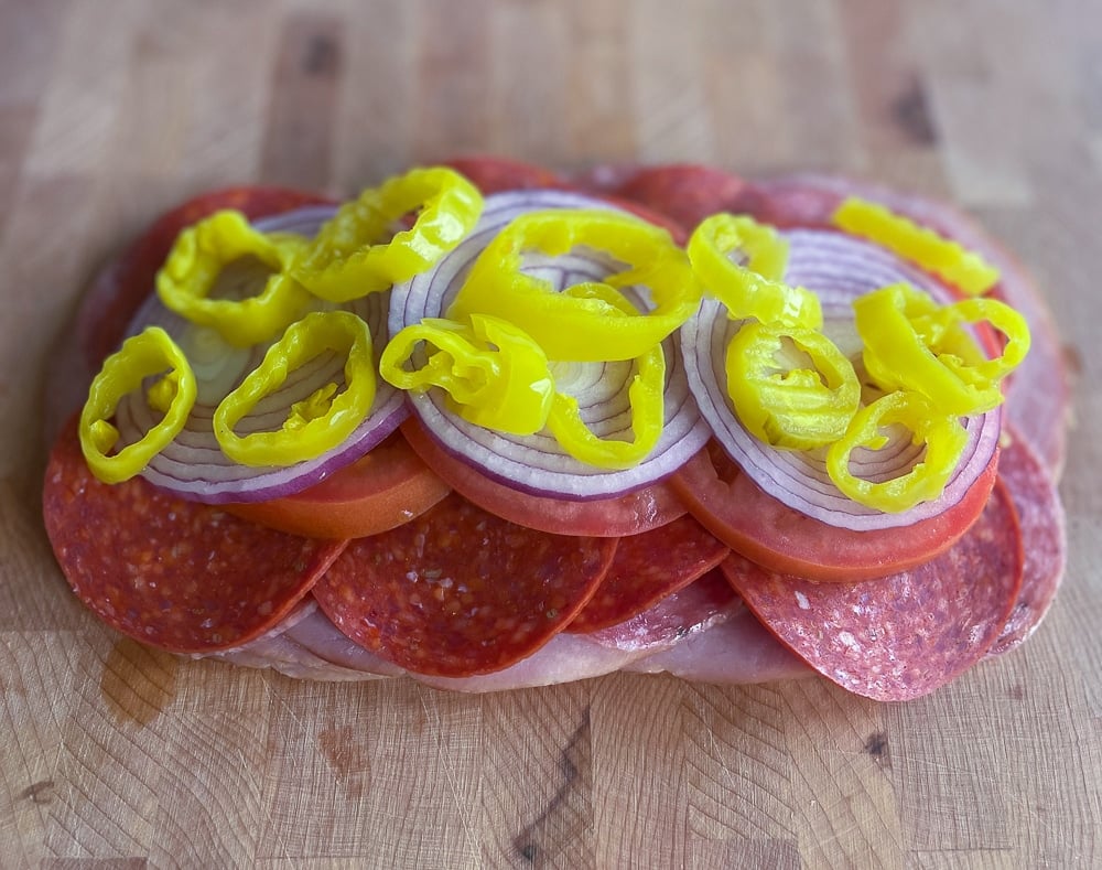Close-up view of thinly sliced red onions topped with bright yellow banana pepper rings, a key step in preparing the flavorful and colorful Italian Grinder Salad recipe.