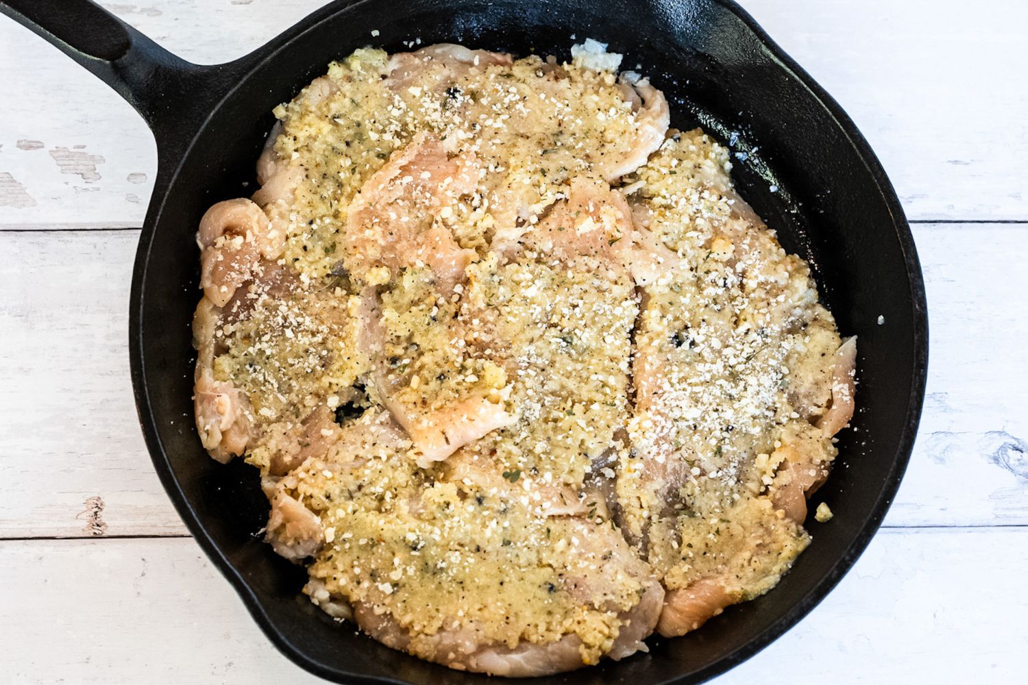 Raw chicken cutlets seasoned with a garlic and parmesan mixture, arranged in a cast iron skillet before baking in the oven.