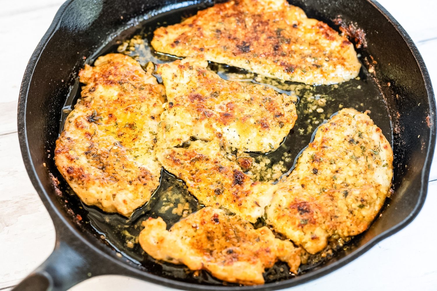 Garlic Parmesan Chicken Cutlets cooked to perfection in a cast iron skillet, seasoned and ready to serve, set against a clean white background.