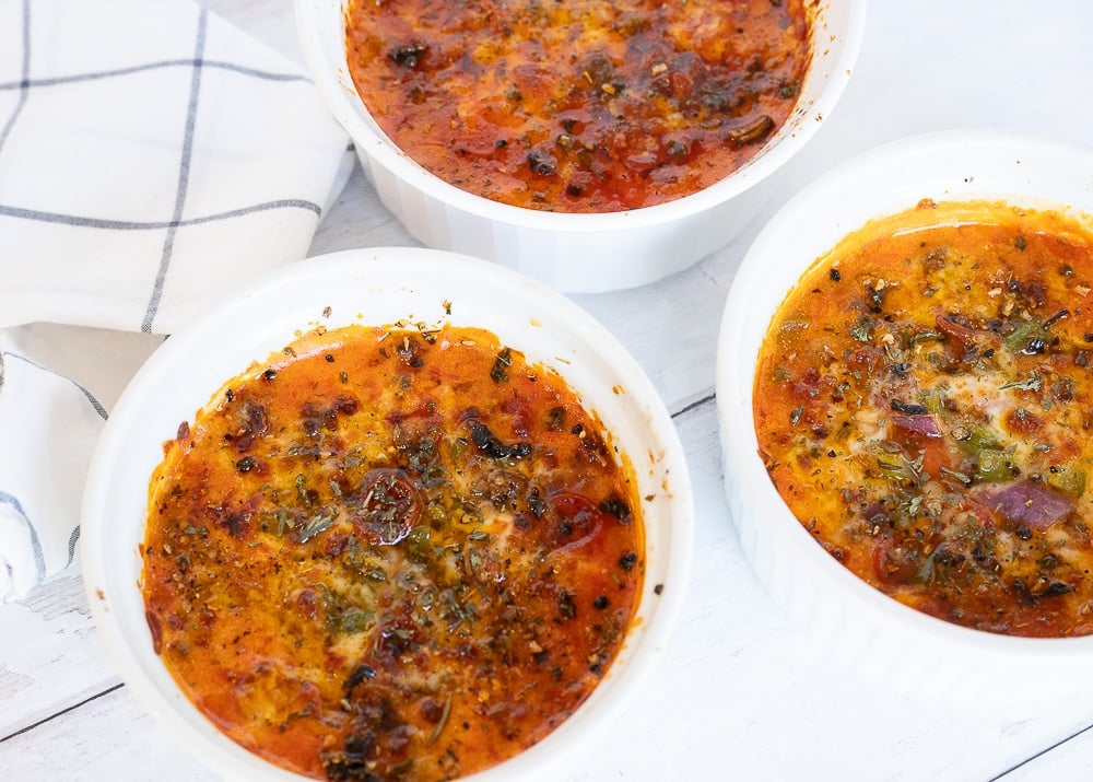 Three low-carb pizza bowls baked in round dishes made with melted cheese, tomato sauce, ground meat, bell peppers, and herbs on a white surface.
