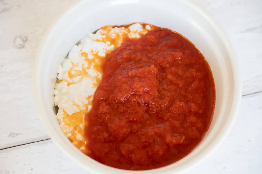 Close-up image of a mouthwatering pizza bowl made with seasoned marinara sauce and melted cottage cheese in a white ceramic dish.