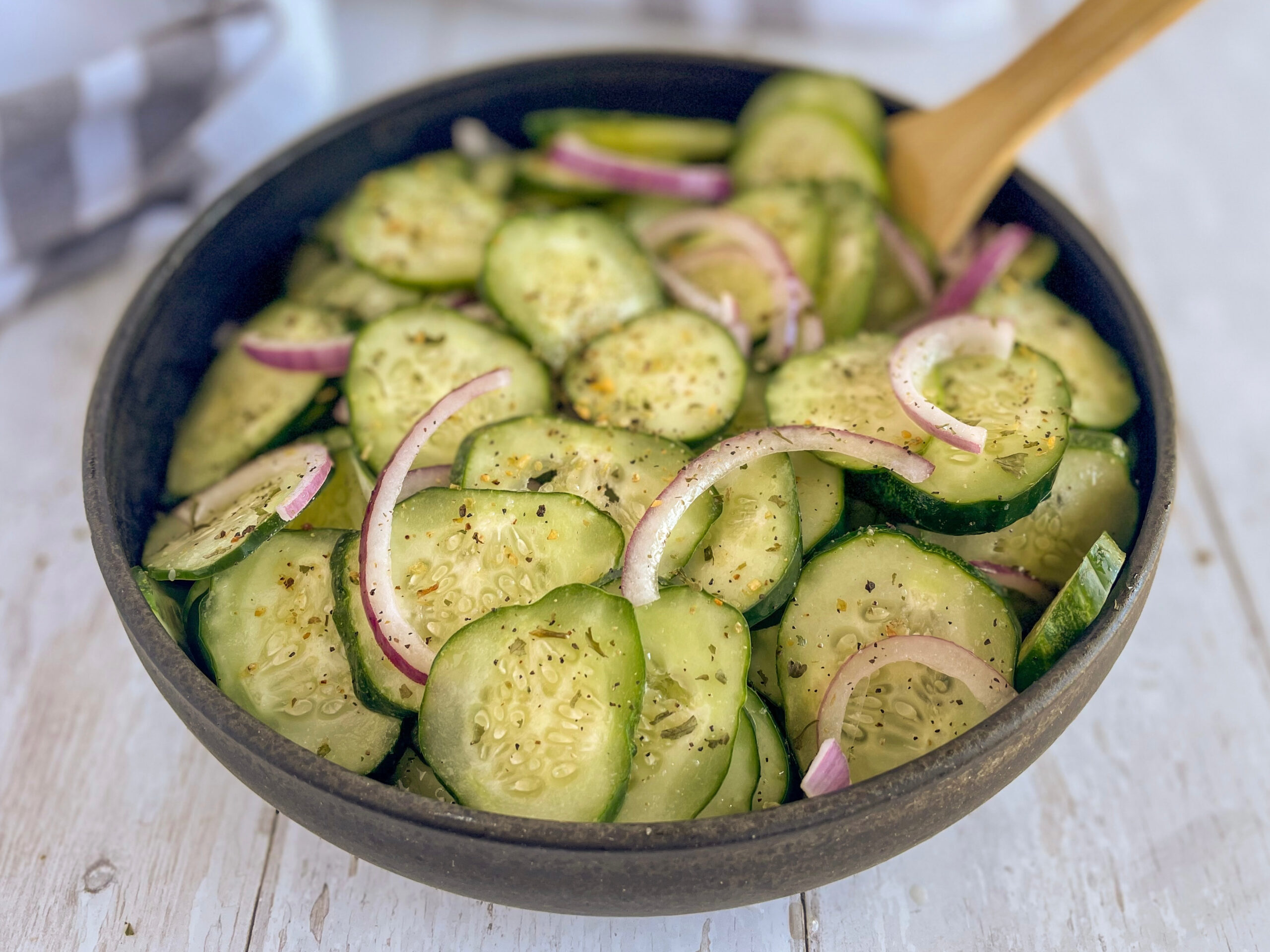 A close-up horizontal image of a finished keto cucumber onion salad in a black bowl, showing crisp cucumbers, thinly sliced red onions, and a tangy vinegar dressing.